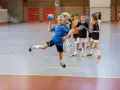Dziewczynka w skoku wykonuje kozłowanie w piłce ręcznej, podczas gdy inni gracze czekają na swoją kolej.