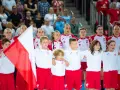 Młode zawodniczki i zawodnicy w strojach reprezentacji Polski, z biało-czerwoną flagą, przed meczem piłka ręczna kobiet mistrzostwa świata.