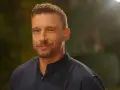 Uśmiechnięty Jakub Wojnowski w granatowej koszuli, w tle rozmyte światła i zieleń.