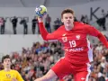 Jan Czuwara w akcji, rzuca piłką do bramki. Zawodnik w czerwonej koszulce z numerem 19.