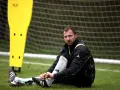Bartosz Dudek, piłkarz, siedzi na murawie, wiążąc sznurówki butów. Obok niego żółta tyczka treningowa.