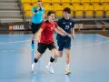 Jakub Smoliński w czerwonej koszulce z numerem 14 biegnie z piłką ręczną, obok zawodnik w granatowej koszulce z numerem 29.