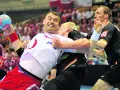 Gracz w białej koszulce z piłką ręczną próbuje wykonać rzut karny, podczas gdy przeciwnik próbuje go zatrzymać.