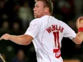 Damian Wleklak, numer 11, w białej koszulce z czerwonymi detalami, przygotowuje się do rzutu piłką ręczną.
