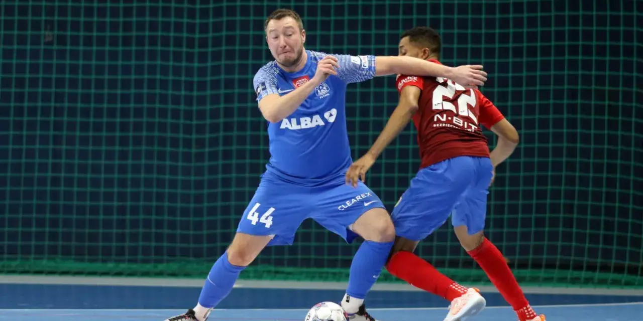 Jakub Grzybowski w akcji, walczy o piłkę z przeciwnikiem na boisku futsalowym.