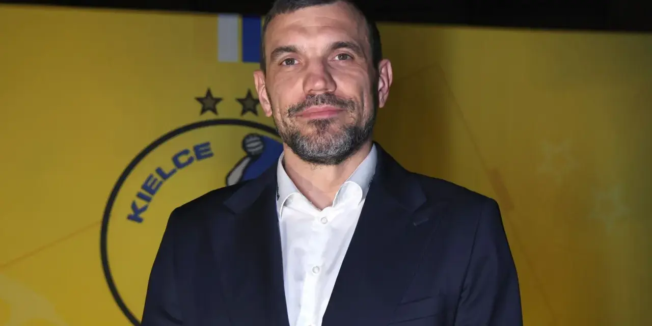 Michał Jurecki w garniturze na tle żółtej ściany z logo "Kielce".