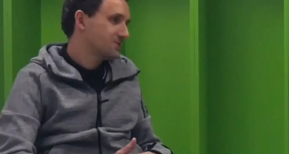 Artur Sadowski w szarej bluzie z kapturem siedzi na tle zielonych ścian, opowiadając o swoich pasjach.