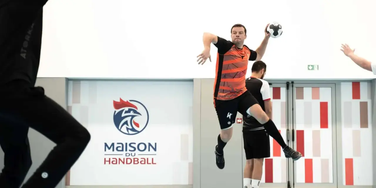 Piłkarz ręczny, niczym szczypiornista, wyskakuje do rzutu. W tle logo "Maison du Handball".