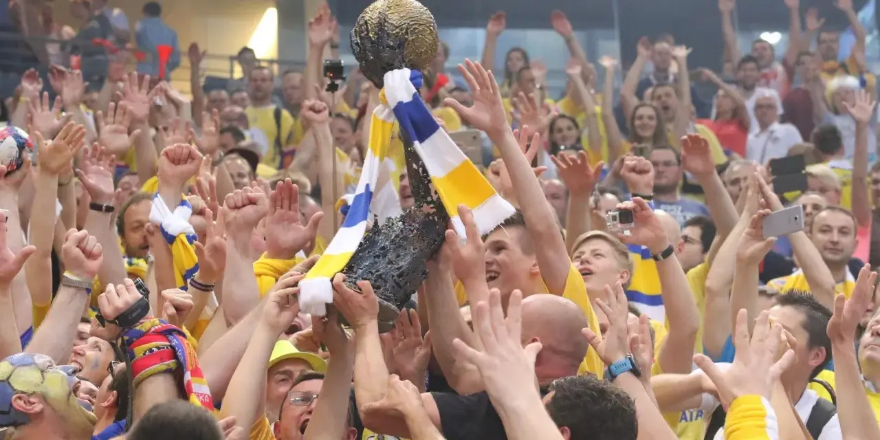 Tłum świętuje zwycięstwo, unosząc puchar. Kibice w żółto-niebieskich barwach, jak na meczach kielce liga mistrzów, cieszą się z sukcesu.