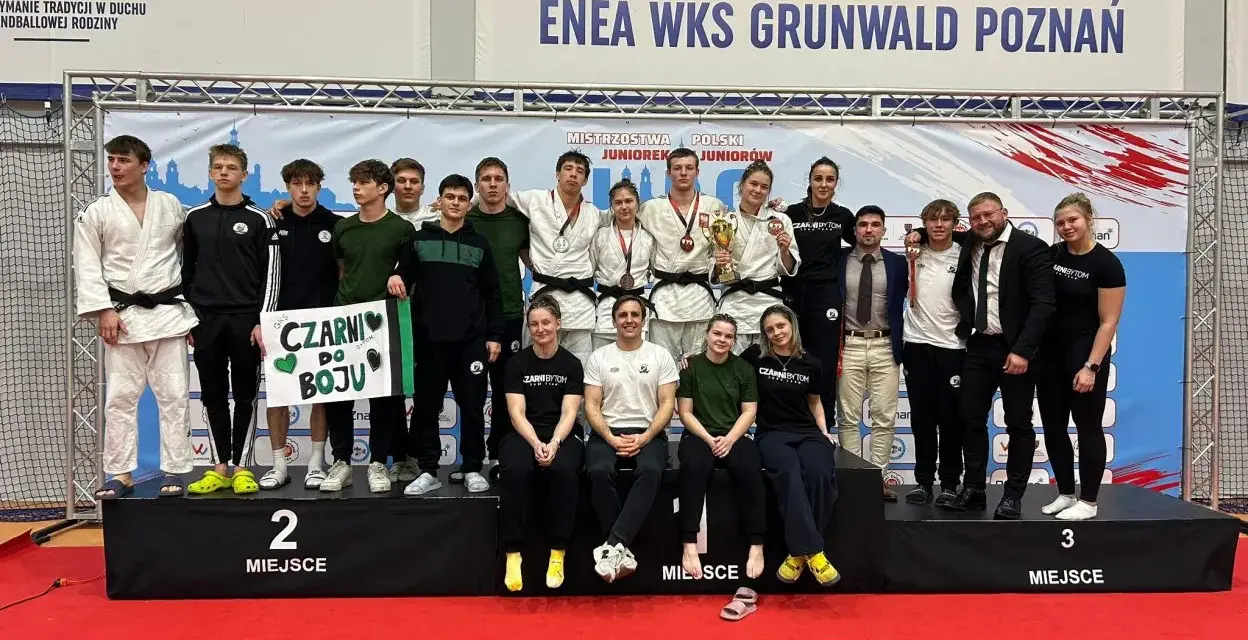 Młodzi sportowcy świętują sukces na mistrzostwa polski juniorów. Drużyna z transparentem "Czarni do boju" pozuje na podium.