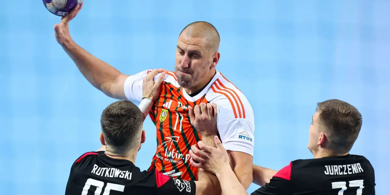 Gracz MKS Piotrkowianin z piłką w ręku, otoczony przez obrońców.