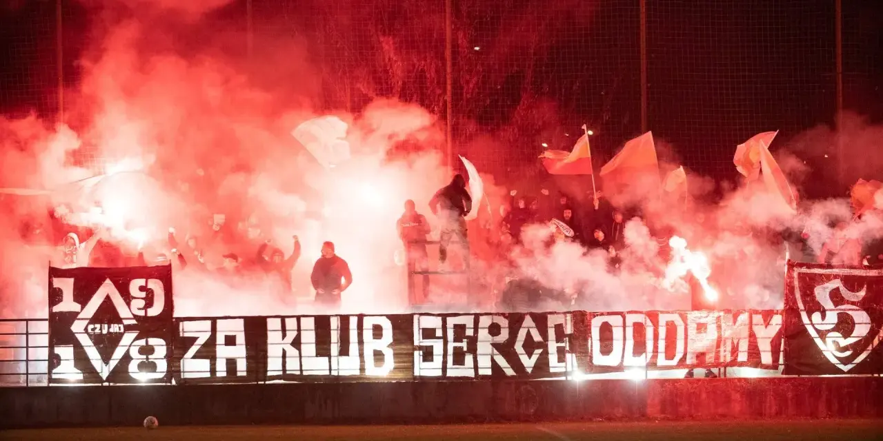 Fani z piłą ręczną, czuwaj przemyśl! Tłum kibiców z racami i flagami tworzy czerwony dym.