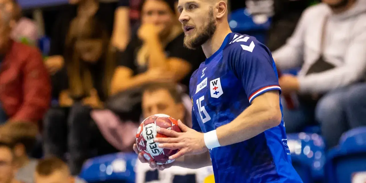 Mateusz Jachlewski, szczypiornista w niebieskiej koszulce z numerem 15, trzyma piłkę do piłki ręcznej.