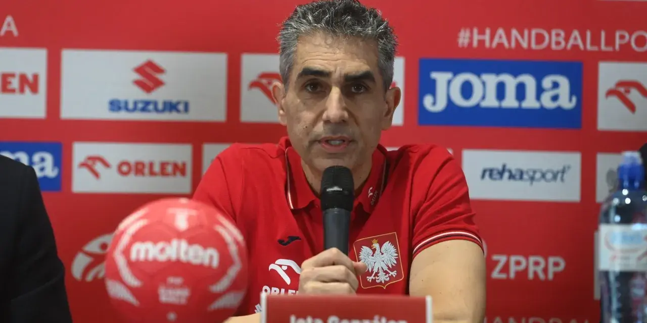 Jota González, trener reprezentacji Polski w piłce ręcznej, przemawia do mikrofonu. Obok niego czerwona piłka.