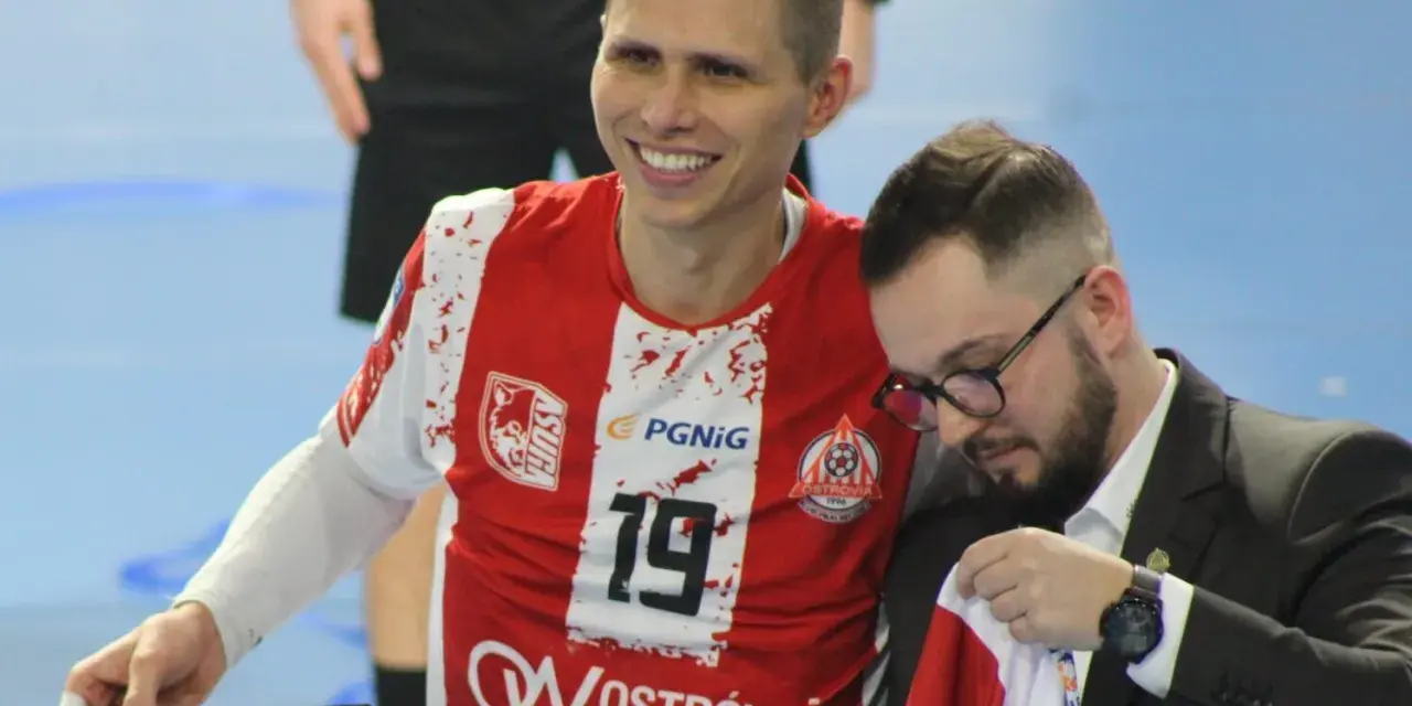 Uśmiechnięty Bartłomiej Tomczak w czerwonej koszulce z numerem 19, obok niego mężczyzna w garniturze.