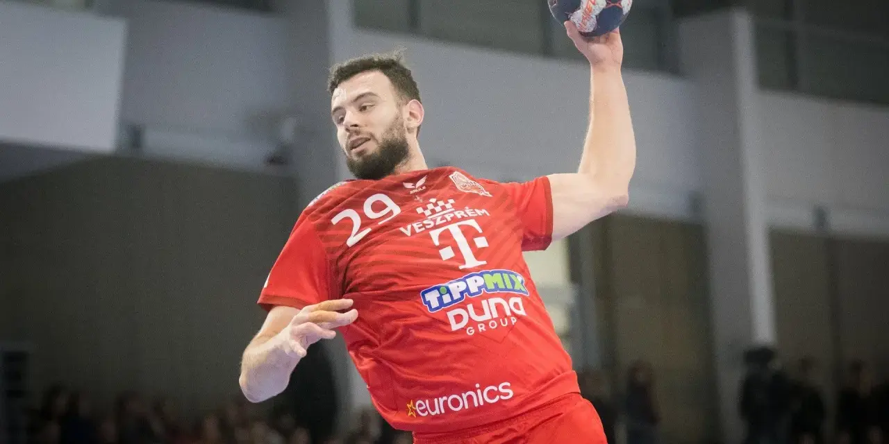 Piłkarz ręczny Nedim Remili w czerwonej koszulce z numerem 29, z piłką w dłoni, gotowy do rzutu.