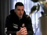 Maciej Pilitowski w czarnej bluzie z orłem i logiem Suzuki, z dłońmi złożonymi na stole, w tle zasłony i rośliny.