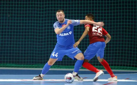 Jakub Grzybowski w akcji, walczy o piłkę z przeciwnikiem na boisku futsalowym.