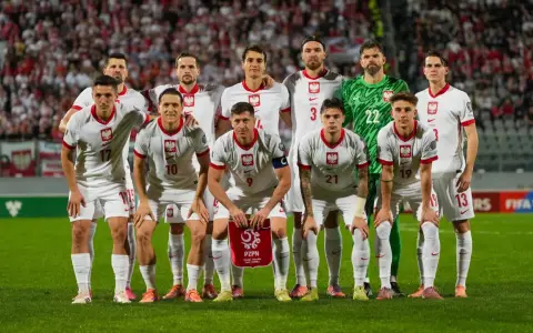 Reprezentacja Polski zawodnicy w białych strojach, gotowi do gry. Na murawie widać dumę i determinację.