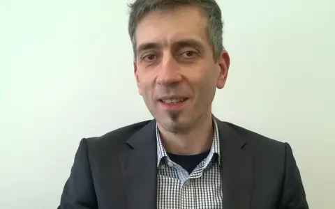 Maciej Kasprzak w czarnym garniturze i koszuli w kratę, z charakterystyczną bródką.