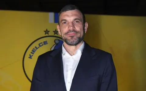 Michał Jurecki w garniturze na tle żółtej ściany z logo "Kielce".
