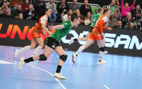 Zawodniczka w zielonej koszulce krzyczy z radości podczas meczu super ligi kobiet. Obok biegnie rywalka w pomarańczowym stroju.