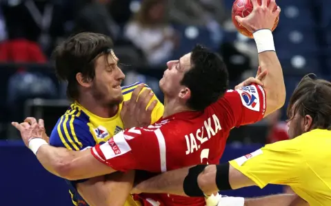 Zacięta walka w meczu polska szwecja piłka ręczna. Zawodnicy walczą o piłkę, jeden w czerwonej koszulce z napisem Jaszka, drugi w żółtej.
