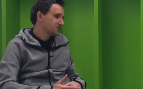 Artur Sadowski w szarej bluzie z kapturem siedzi na tle zielonych ścian, opowiadając o swoich pasjach.