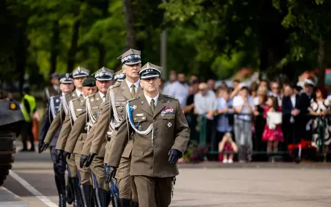 Tomasz Zaręba w mundurze maszeruje w defiladzie wojskowej. W tle widzowie obserwują uroczystość.
