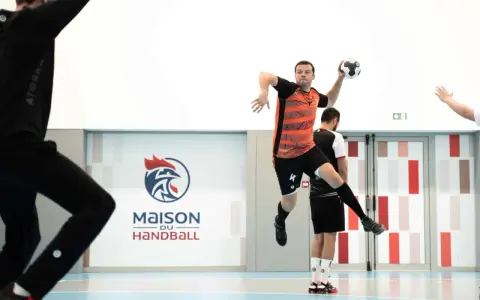 Piłkarz ręczny, niczym szczypiornista, wyskakuje do rzutu. W tle logo "Maison du Handball".