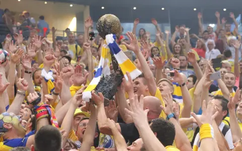 Tłum świętuje zwycięstwo, unosząc puchar. Kibice w żółto-niebieskich barwach, jak na meczach kielce liga mistrzów, cieszą się z sukcesu.
