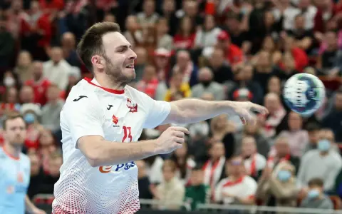 Piłkarz ręczny Polski w akcji, rzuca piłkę. W tle widać trybuny z kibicami, którzy dopingują swoją drużynę w meczu przeciwko Iranowi.