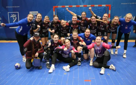 Drużyna piłki ręcznej KPR Bukowsko Dopiewo świętuje zwycięstwo. Radosne zawodniczki w strojach sportowych, z numerami na koszulkach, pozują do zdjęcia z trenerem.