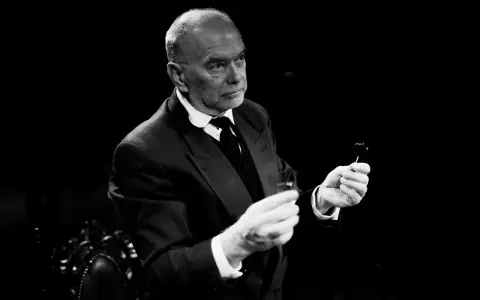 Piotr Wyszomirski w eleganckim garniturze, trzymający w dłoniach kieliszek i coś na patyczku.