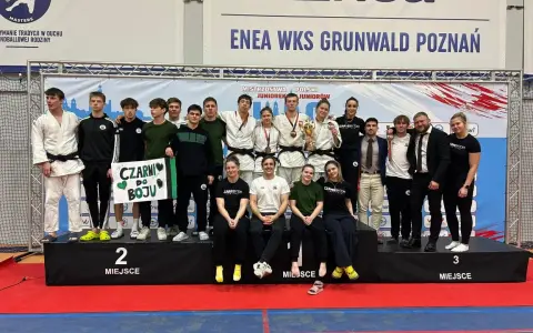Młodzi sportowcy świętują sukces na mistrzostwa polski juniorów. Drużyna z transparentem "Czarni do boju" pozuje na podium.