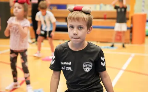 Chłopiec z zabawką na głowie, w koszulce KS Bysstra, podczas zajęć sportowych.