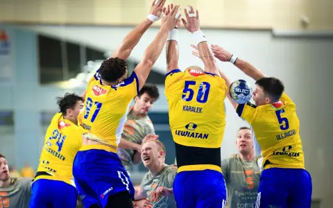 Piłkarze ręczni w żółtych koszulkach, prawdopodobnie z drużyny Kielc, świętują zwycięstwo nad Aalborgiem.