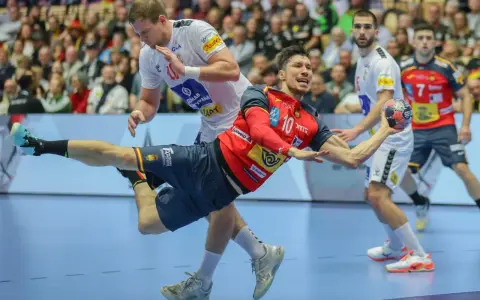Piłkarz ręczny Hiszpanii w czerwonej koszulce z numerem 10 wykonuje rzut. W tle inny zawodnik i kibice.