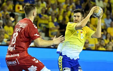 Piłkarz Aalborg Handball w żółtej koszulce rzuca piłkę, obok zawodnik w czerwonej.