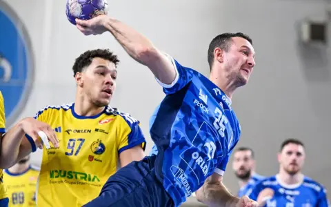 Gracz w niebieskiej koszulce rzuca piłkę, podczas gdy przeciwnik w żółtej koszulce z numerem 97 próbuje go zablokować. Emocjonujący mecz piłka ręczna liga mistrzów.
