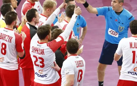 Polska kadra piłka ręczna świętuje zwycięstwo. Zawodnicy w białych strojach z czerwonymi detalami, z numerami 18, 23 i 15, cieszą się z sukcesu.