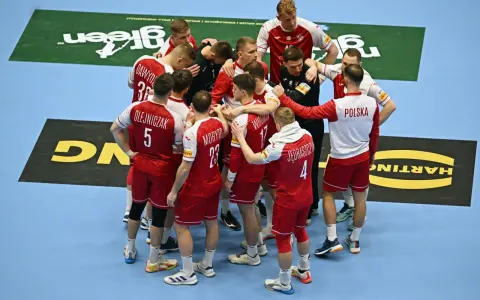 Drużyna piłkarzy ręcznych Polski w czerwonych strojach z białymi detalami, zjednoczona w kółku. To kluczowy moment przed meczem, być może decydującym o dalszych losach w mistrzostwach świata.