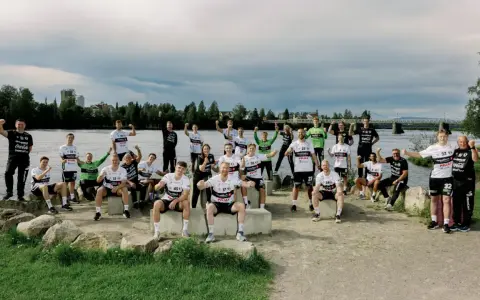 Drużyna Elverum Handball świętuje nad rzeką, pozując do wspólnego zdjęcia w sportowych strojach.