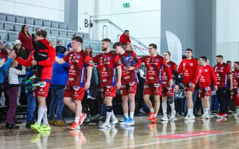 Drużyna kwidzyn piłka ręczna w czerwonych strojach wchodzi na halę, pozdrawiając kibiców.