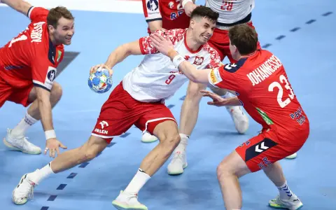 Gracz w białej koszulce z numerem 9 próbuje rzucić piłkę, podczas gdy obrońca w czerwonej koszulce z numerem 23 stara się mu przeszkodzić. Emocjonująca akcja w meczu piłki ręcznej.