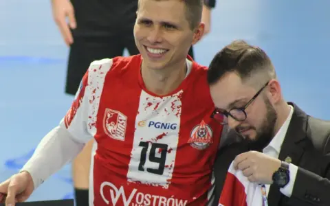 Uśmiechnięty Bartłomiej Tomczak w czerwonej koszulce z numerem 19, obok niego mężczyzna w garniturze.