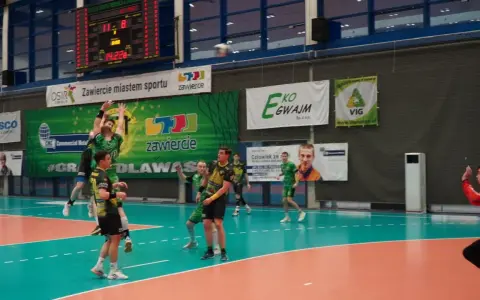 Mecz siatkówki w Zawierciu. Zawodnicy w zielonych strojach walczą o piłkę pod koszem.