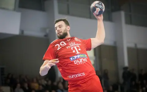Piłkarz ręczny Nedim Remili w czerwonej koszulce z numerem 29, z piłką w dłoni, gotowy do rzutu.