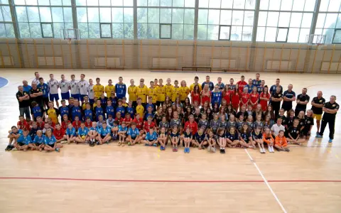 Drużyna Olimp Grodków na hali sportowej. Duża grupa dzieci i młodzieży w strojach sportowych pozuje do wspólnego zdjęcia.