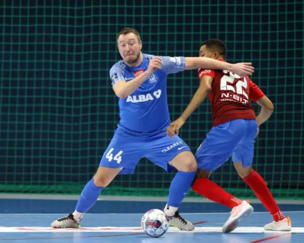 Jakub Grzybowski w akcji, walczy o piłkę z przeciwnikiem na boisku futsalowym.